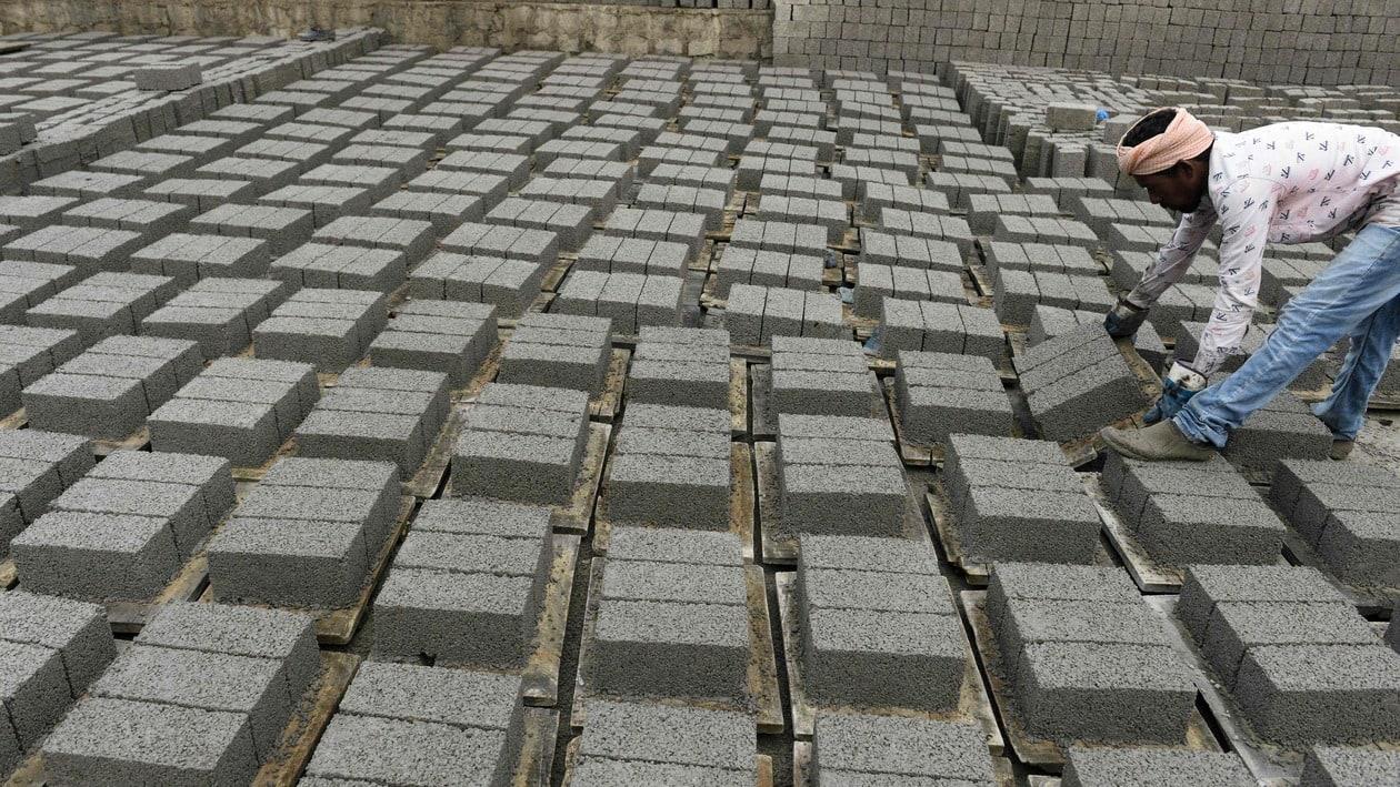 A labourer arranges cement bricks for drying at a manufacturing unit on the outskirts of Hyderabad on January 15, 2022. (Photo by NOAH SEELAM / AFP)