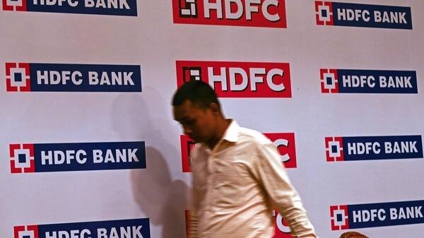 A man walks past logos of Housing Development Finance Corporation (HDFC) and HDFC Bank at an event in Mumbai on April 4, 2022. - India's largest private bank will merge with its largest mortgage lender to become a $237 billion financial giant, both companies said, as low interest rates send demand for home loans soaring. (Photo by Indranil MUKHERJEE / AFP)