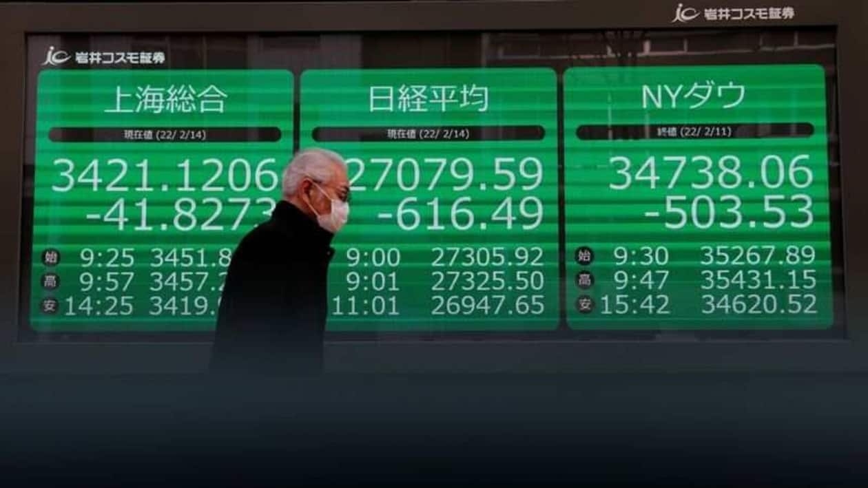 A man wearing a protective face mask, amid the coronavirus disease (COVID-19) pandemic, walks past a screen showing Shanghai Composite index, Nikkei index and Dow Jones Industrial Average outside a brokerage in Tokyo, Japan, February 14, 2022. REUTERS/Kim Kyung-Hoon