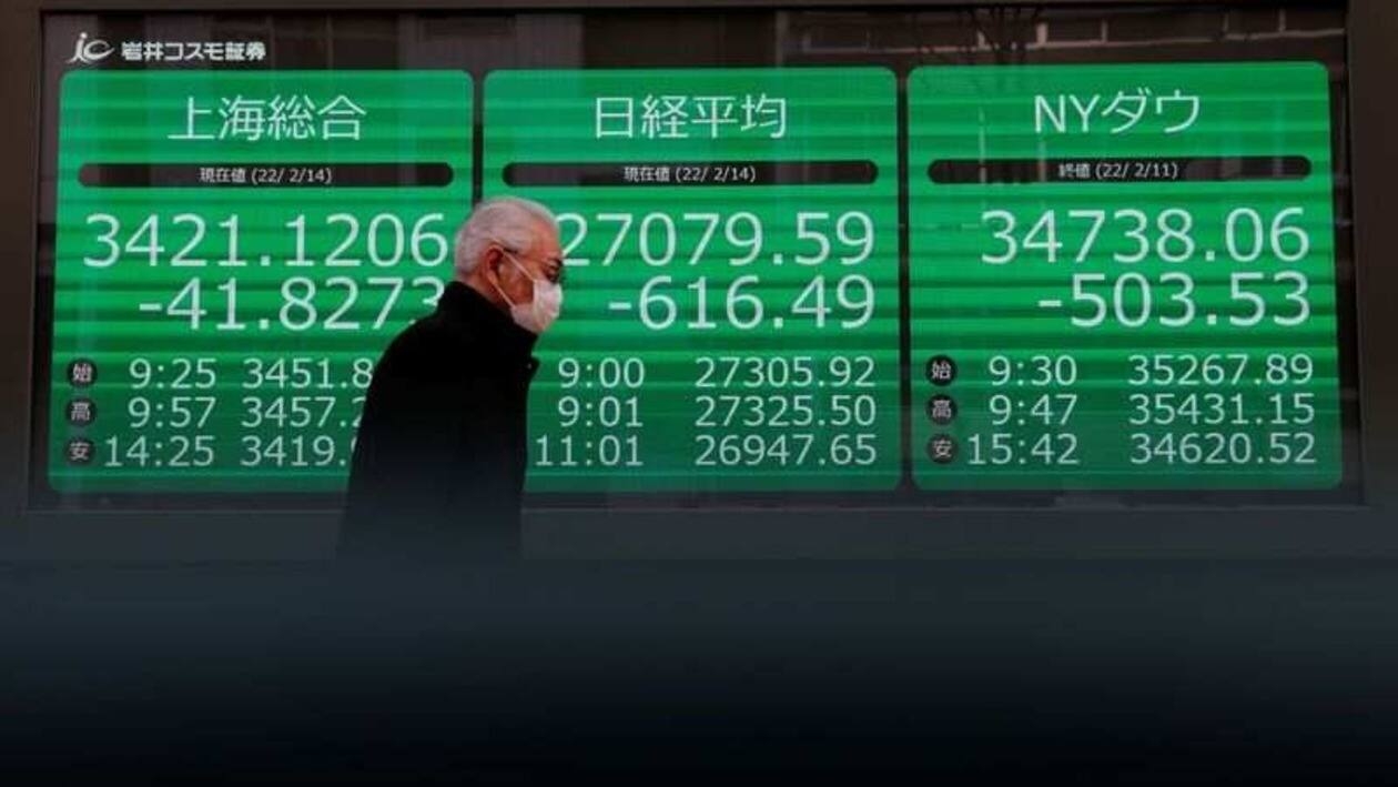 A man wearing a protective face mask, amid the coronavirus disease (COVID-19) pandemic, walks past a screen showing Shanghai Composite index, Nikkei index and Dow Jones Industrial Average outside a brokerage in Tokyo, Japan, February 14, 2022. REUTERS/Kim Kyung-Hoon