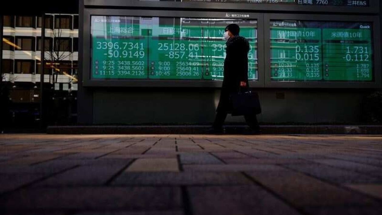 A man wearing a protective mask, amid the coronavirus disease (COVID-19) outbreak, walks past an electronic board displaying Shanghai Composite index, Nikkei index and Dow Jones Industrial Average outside a brokerage in Tokyo, Japan, March 7, 2022. REUTERS/Kim Kyung-Hoon