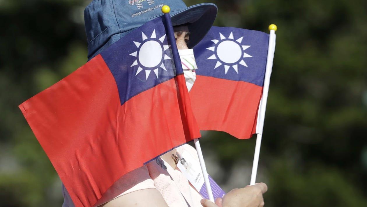 FILE - In this Sunday, Oct. 10, 2021, file photo, a woman holds up Taiwan national flags during National Day celebrations in front of the Presidential Building in Taipei, Taiwan.  In 1997, Beijing grumbled but swallowed its irritation when then-Speaker Newt Gingrich of the U.S. House of Representatives visited Taiwan.   A quarter-century later, news reports that the current speaker, Nancy Pelosi, might visit Taiwan, Beijing is warning of “forceful measures” including military action if she does.(AP Photo/Chiang Ying-ying, File)