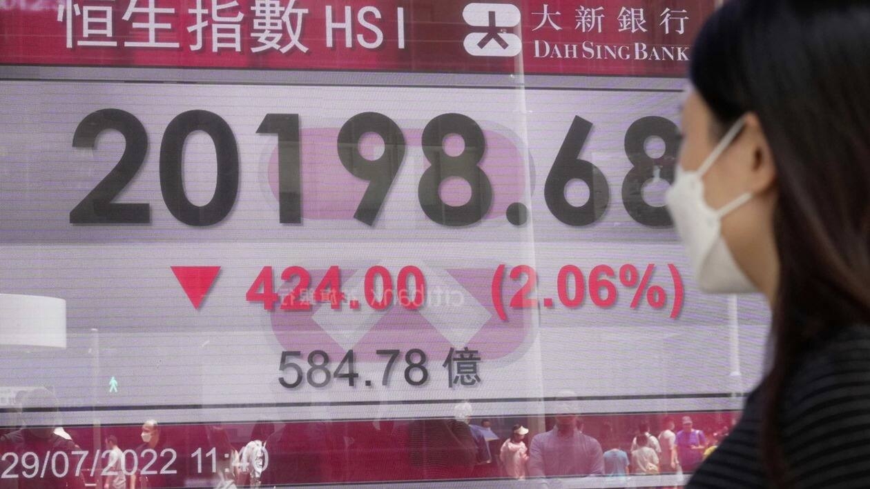 A woman wearing a face mask walks past a bank's electronic board showing the Hong Kong share index in Hong Kong, Friday, July 29, 2022. Asian shares mostly rose Friday, following a broad rally on Wall Street as investors grew more optimistic that the U.S. Federal Reserve may temper its aggressive interest rate hikes aimed at taming inflation. (AP Photo/Kin Cheung)