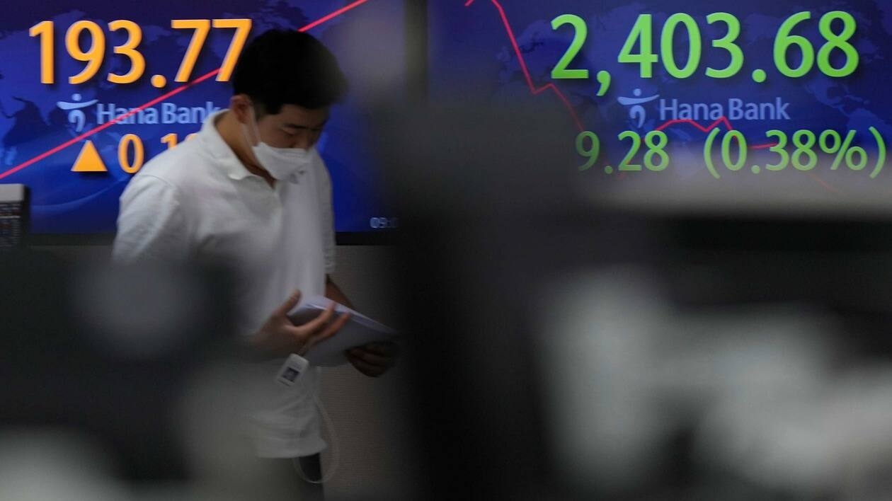 A currency trader walks near the screens showing the Korea Composite Stock Price Index (KOSPI), right, and the foreign exchange rate at a foreign exchange dealing room in Seoul, South Korea, Wednesday, July 27, 2022. Asian stock markets followed Wall Street lower Wednesday as traders prepared for a possible sharp interest rate hike from the Federal Reserve to cool inflation. (AP Photo/Lee Jin-man)