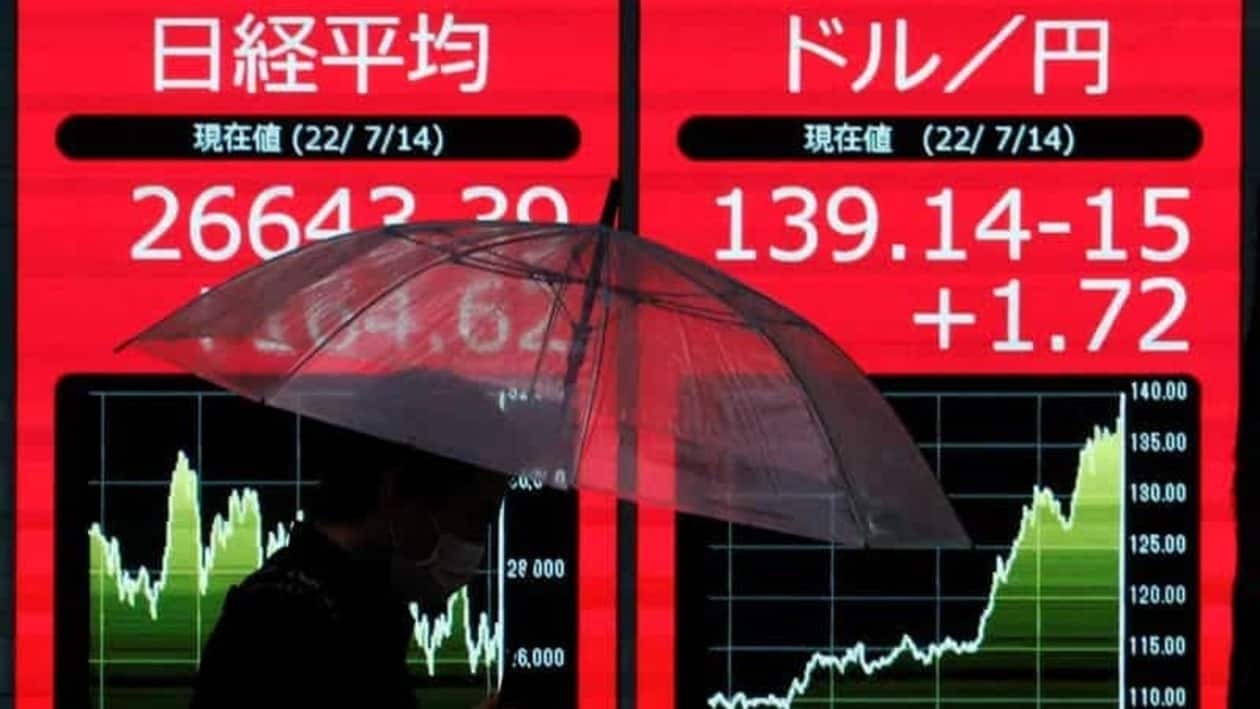 FILE PHOTO: A man holding an umbrella is silhouetted as he walks in front of an electric monitor displaying the Japanese yen exchange rate against the U.S. dollar  and Nikkei share average in Tokyo, Japan July 14, 2022  REUTERS/Issei Kato