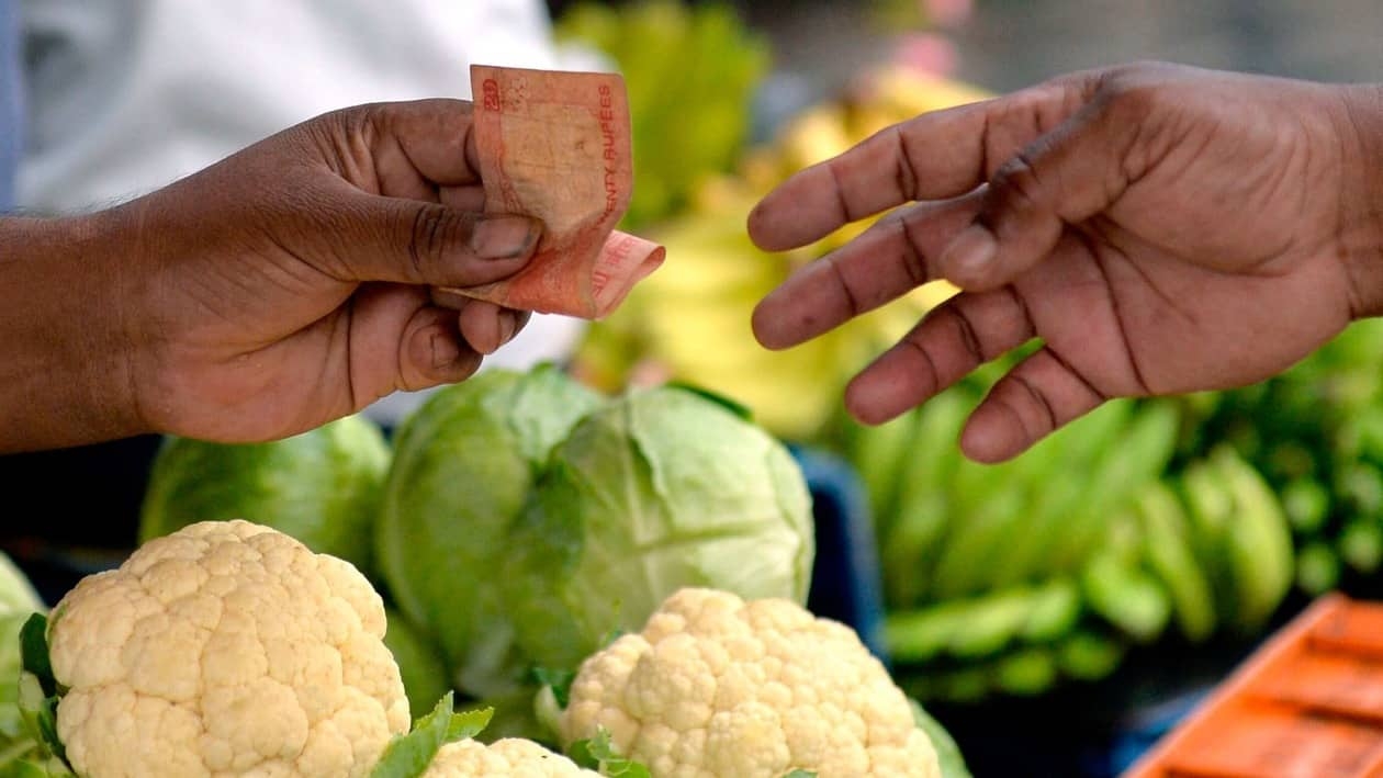 A vegetable vendor (L) hands a twenty Indian Rupee currency note change to a customer in Mumbai on July 19, 2022. - The Indian rupee fell to more than 80 per US dollar for the first time on record on July 19, as the greenback extended its rally and foreign capital outflows intensified. (Photo by INDRANIL MUKHERJEE / AFP)