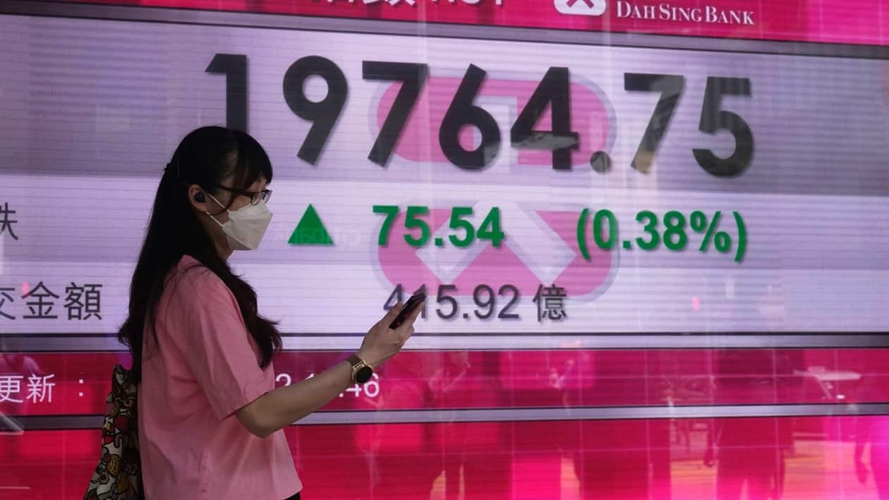 A woman wearing a face mask walks past a bank's electronic board showing the Hong Kong share index in Hong Kong, Wednesday, Aug. 3, 2022. Asian stock markets rose Wednesday as traders watched for signs trade might be disrupted by U.S.-Chinese tension over an American lawmaker's visit to Taiwan. (AP Photo/Kin Cheung)