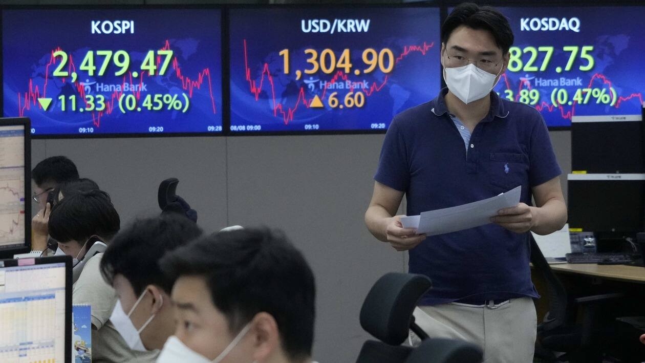A currency trader passes by screens showing the Korea Composite Stock Price Index (KOSPI), left, and the exchange rate of South Korean won against the U.S. dollar, center, at the foreign exchange dealing room of the KEB Hana Bank headquarters in Seoul, South Korea, Monday, Aug. 8, 2022. Asian stocks were mixed Monday after strong U.S. jobs data cleared the way for more interest rate hikes and Chinese exports rose by double digits. (AP Photo/Ahn Young-joon)