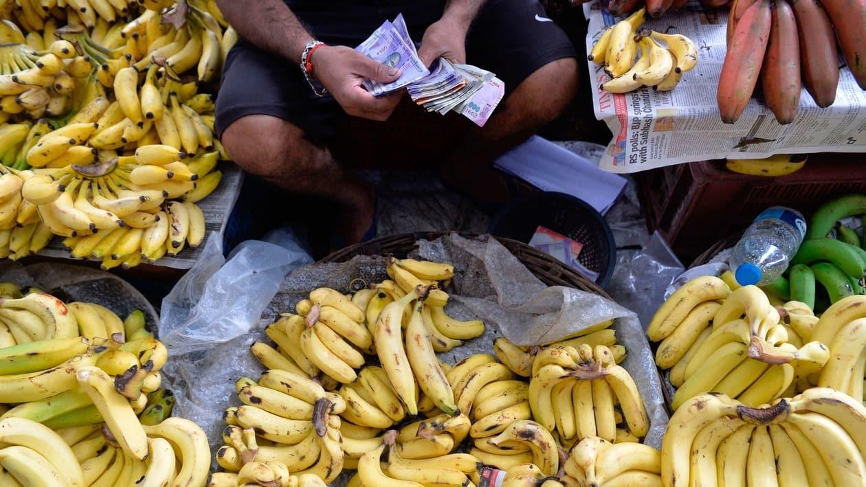 A fruit vendor counts a wad of Indian Rupee currency notes for payment at his roadside stall in Mumbai on July 19, 2022. - The Indian rupee fell to more than 80 per US dollar for the first time on record on July 19, as the greenback extended its rally and foreign capital outflows intensified. (Photo by INDRANIL MUKHERJEE / AFP)
