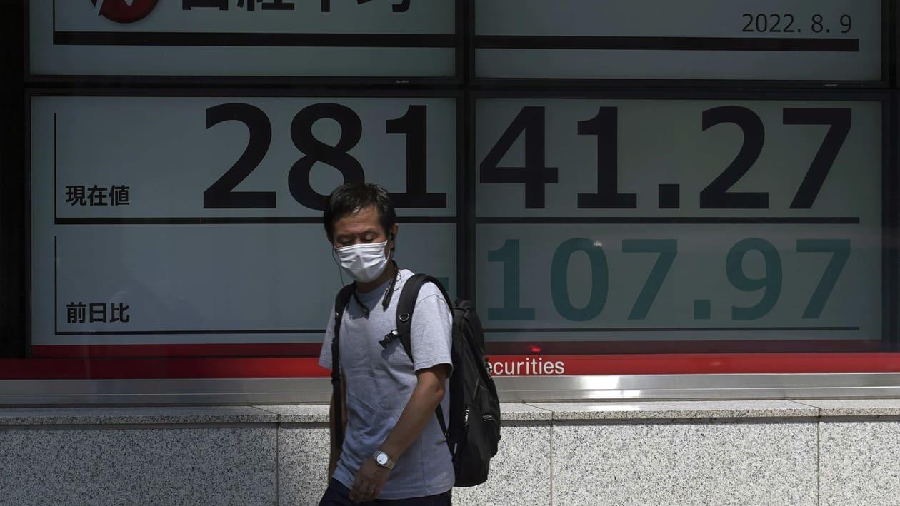 A person wearing a protective mask walks in front of an electronic stock board showing Japan's Nikkei 225 index at a securities firm Tuesday, Aug. 9, 2022, in Tokyo. Asian shares mostly declined Tuesday amid a global fall in technology shares, including Japan's SoftBank, which has reported hefty losses caused by the market downturn. (AP Photo/Eugene Hoshiko)