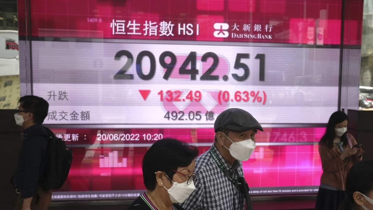 People wearing face masks walk past a bank's electronic board showing the Hong Kong share index in Hong Kong, Monday, June 20, 2022. Asian markets were mostly lower in cautious trading Monday ahead of a federal holiday in the U.S. (AP Photo/Kin Cheung)