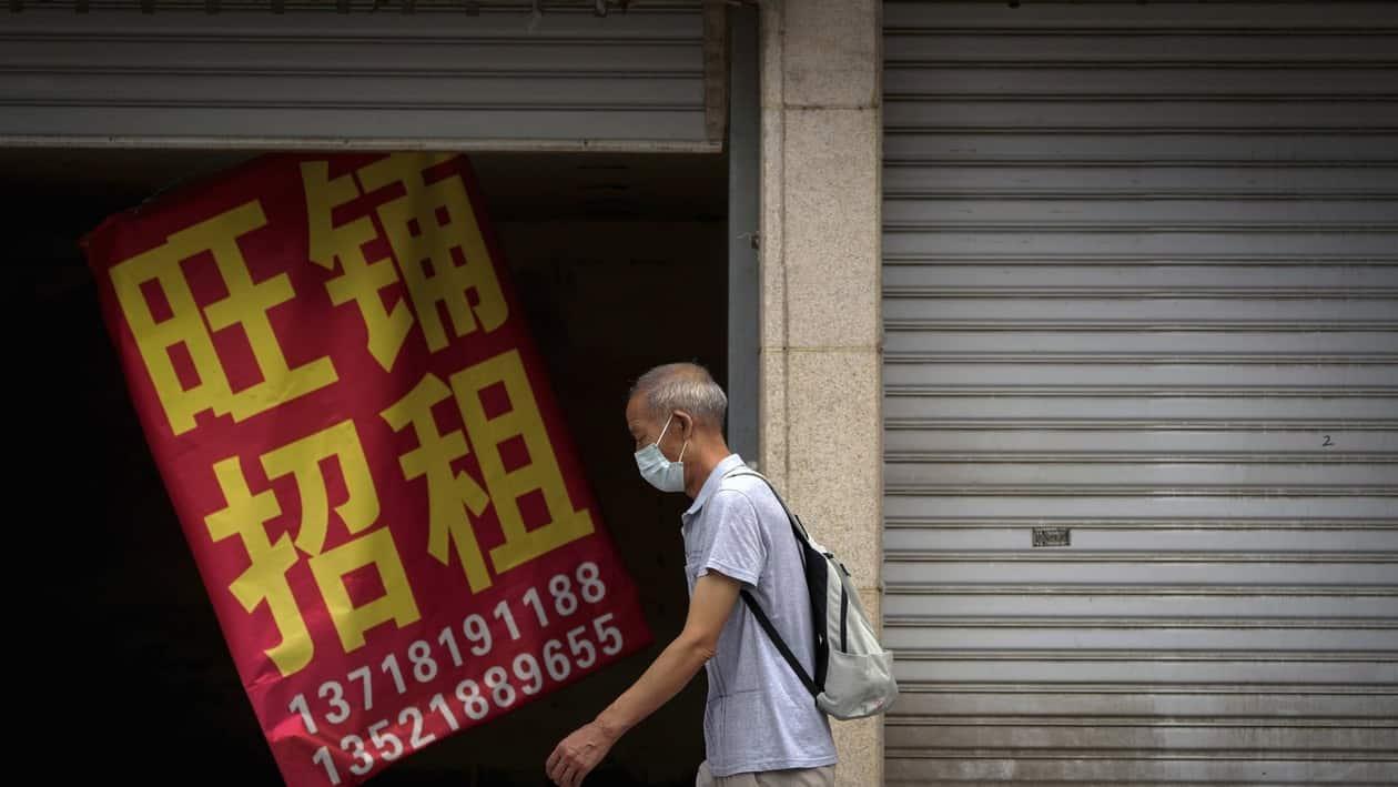 A man wearing a face mask walks by a banner that reads Prosperous shop for rent hangs on a vacant shop lot in Beijing, Wednesday, Aug. 17, 2022. Factories in China's southwest have shut down after reservoirs used to generate hydropower ran low in a worsening drought, adding to economic strains at a time when President Xi Jinping is trying to extend his position in power. (AP Photo/Andy Wong)