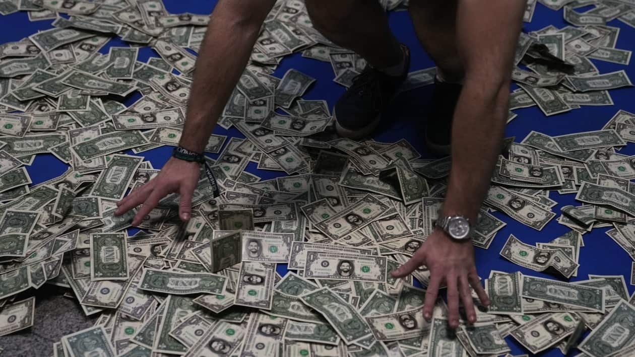 A man gathers fake dollar banknotes to throw up in the air at a cryptocurrency event in Madrid, Spain, Saturday, Aug. 27, 2022. Spanish financial authorities are planning to keep a close eye on a major cryptocurrency metaverse event being organized in Madrid this weekend. The CNMV stock market regulator this week warned that neither the organizers of the event, Mundocrypto, nor the sponsors have authorization to provide investment services or gather funds. (AP Photo/Paul White)
