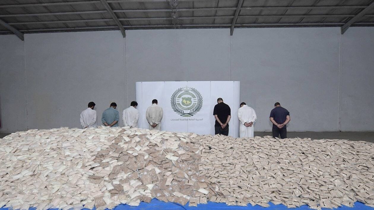 An handout picture released by the Saudi Interior Ministry on August 31, 2022, shows handcuffed suspects and bags of amphetamine pills on display at a warehouse in a undisclosed location. - Saudi officers thwarted an attempt to smuggle 47 million amphetamine pills into the country, state media reported, describing it as the largest ever drug trafficking operation in the kingdom. Six Syrians and two Pakistanis were arrested in a raid after the pills, concealed in a flour shipment, arrived at a dry port in the capital Riyadh. The report did not specify whether the pills were captagon -- the amphetamine wreaking havoc across the Middle East -- nor did it say where the pills came from. (Photo by SAUDI INTERIOR MINISTRY / AFP)