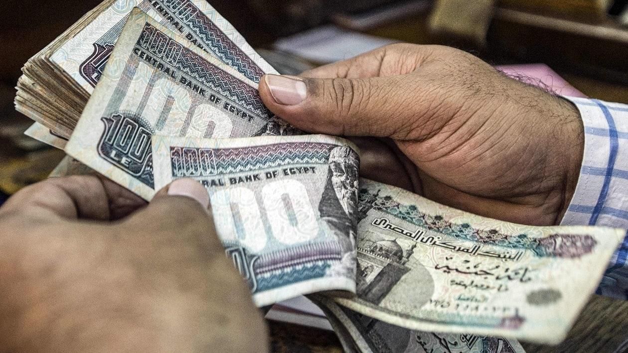 (FILES) In this file a man counts Egyptian pound banknotes at a currency exchange shop in downtown Cairo on November 3, 2016. - Depleted foreign currency reserves are casting a shadow on Egyptian streets, with the government moving to dim lights to free up energy for export. More natural gas exports means more hard currency, a dire need as experts say a new loan from the International Monetary Fund (IMF) � and an adjacent currency liberalisation � is inevitable. (Photo by KHALED DESOUKI / AFP)