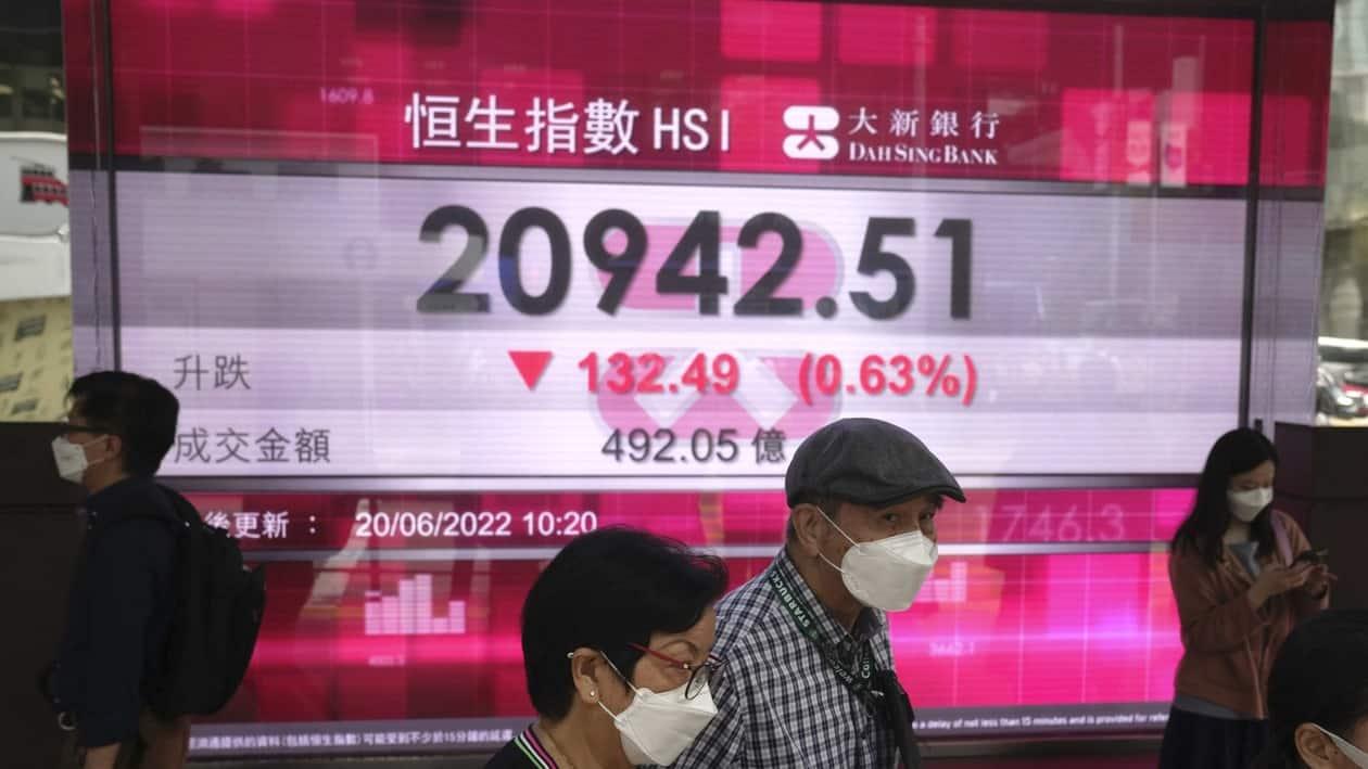 People wearing face masks walk past a bank's electronic board showing the Hong Kong share index in Hong Kong, Monday, June 20, 2022. Asian markets were mostly lower in cautious trading Monday ahead of a federal holiday in the U.S. (AP Photo/Kin Cheung)
