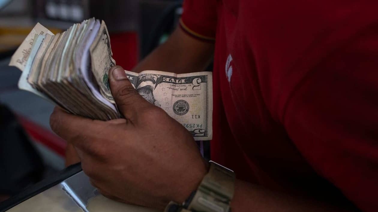 A worker holds a stack of US dollars and Venezuelan bolivares while pumping fuel at a Petroleos de Venezuela SA (PDVSA) gas station in Caracas, Venezuela, on Thursday, Sept. 8, 2022. Venezuela's monthly consumer price index accelerated at its fastest pace so far in 2022, reaching 17.3% in August. Photographer: Gaby Oraa/Bloomberg