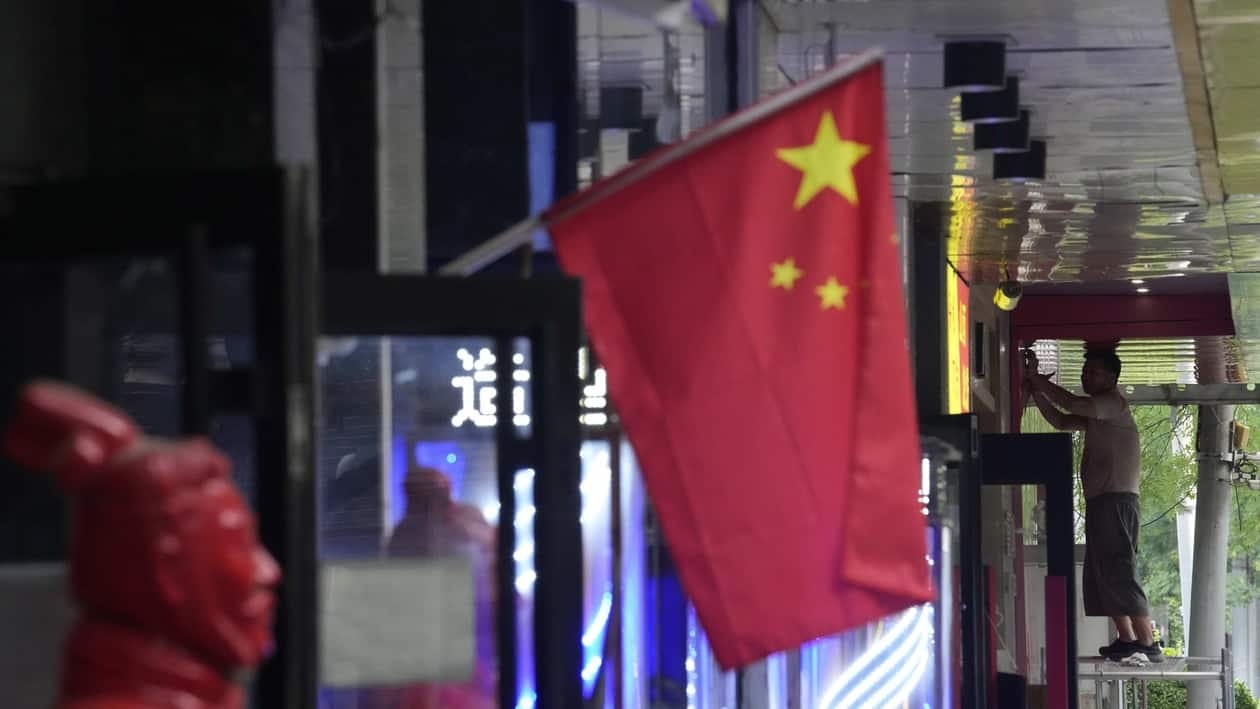 A worker stands on a platform near a Chinese national flag, Friday, July 15, 2022, in Beijing. China's economy contracted in the three months ending in June compared with the previous quarter after Shanghai and other cities shut down to fight coronavirus outbreaks, but the government said a stable recovery is under way after businesses reopened. (AP Photo/Ng Han Guan)