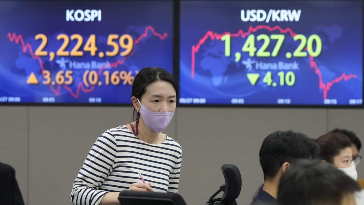 A currency trader passes by screens showing the Korea Composite Stock Price Index (KOSPI), left, and the exchange rate of South Korean won against the U.S. dollar at the foreign exchange dealing room of the KEB Hana Bank headquarters in Seoul, South Korea, Tuesday, Sept. 27, 2022. Stocks were mixed in Asia on Tuesday after closing broadly lower on Wall Street, where the Dow Jones Industrial Average fell into what’s known as a bear market. (AP Photo/Ahn Young-joon)