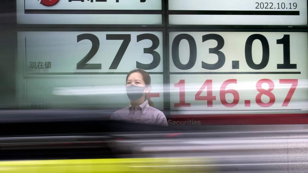 A person wearing a protective mask stands in front of an electronic stock board showing Japan's Nikkei 225 index as a vehicle passing by at a securities firm Wednesday, Oct. 19, 2022, in Tokyo. Asian stock markets were mixed Wednesday after Wall Street rose on strong corporate profit reports. (AP Photo/Eugene Hoshiko)