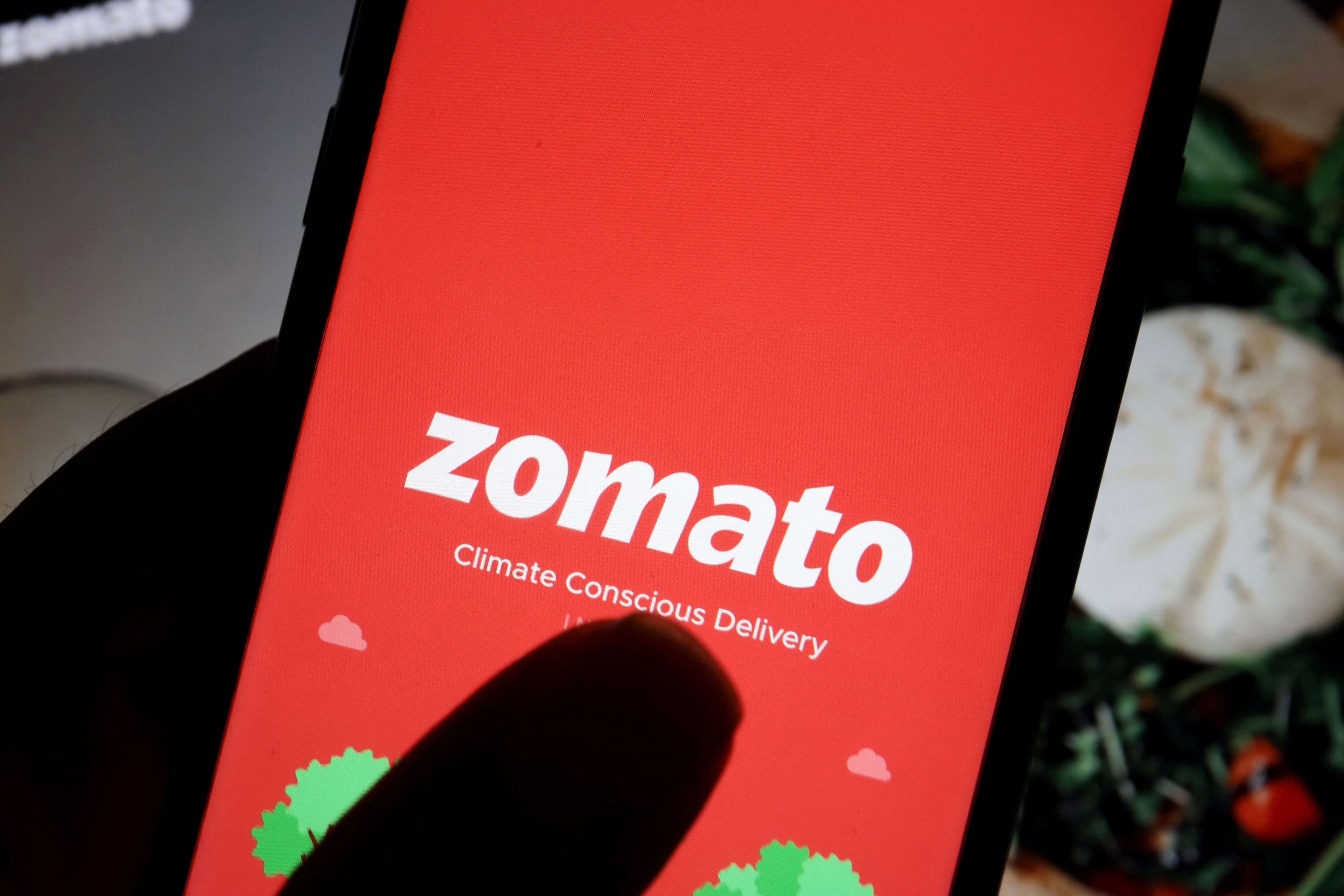 FILE PHOTO: The logo of Indian food delivery company Zomato is seen on its app on a mobile phone displayed in front of its company website in this illustration picture taken July 14, 2021. REUTERS/Florence Lo/Illustration/File Photo