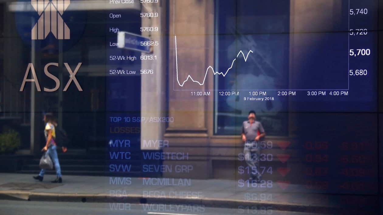 FILE PHOTO: Pedestrians are reflected in a window in front of a board displaying stock prices at the Australian Securities Exchange (ASX) in Sydney, Australia, February 9, 2018.   REUTERS/David Gray/File Photo