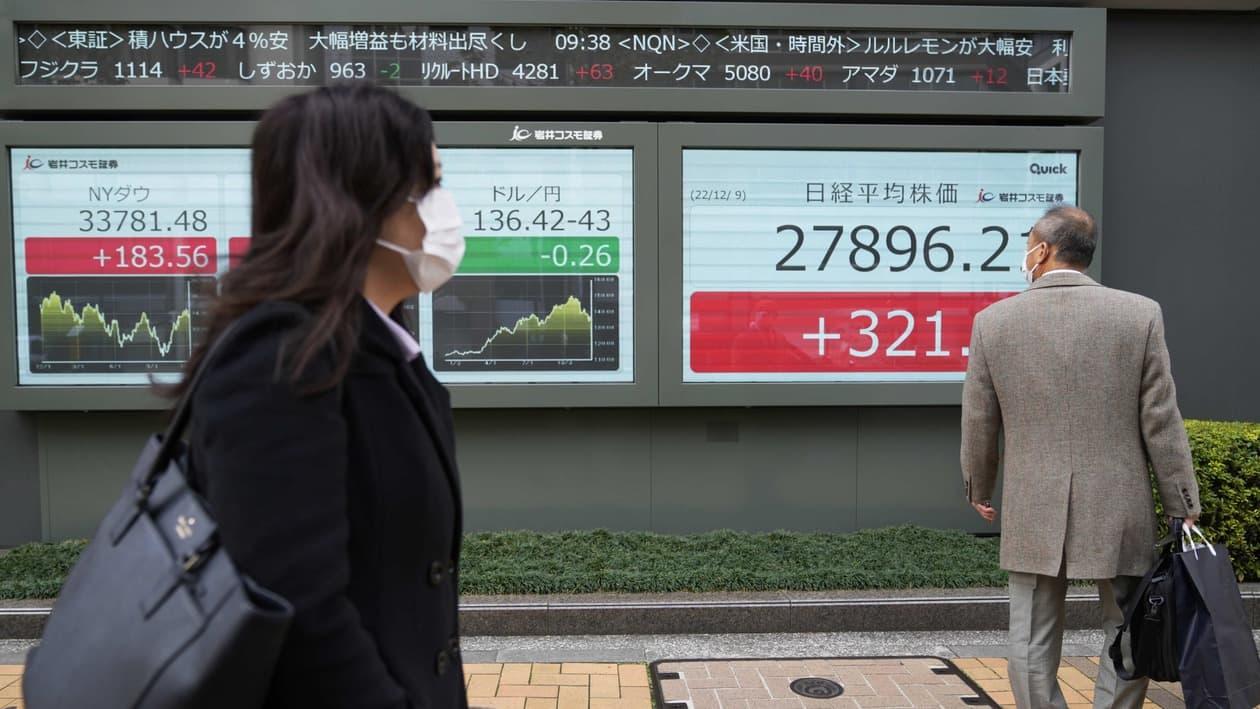 A man looks at the the Dow Jones Industrial Average, far left, and an exchange rate, center, of the Japanese yen against the U.S. dollar as he walks by monitors also showing Japan's Nikkei 225 index, right, at a securities firm in Tokyo, Friday, Dec. 9, 2022. (AP Photo/Hiro Komae)