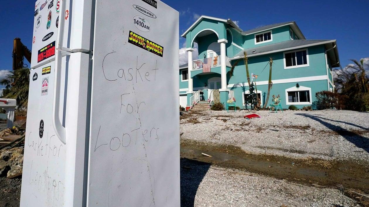 A damaged refrigerator with the words Casket for Looters, written on the side sits next to a home in the aftermath of Hurricane Ian, Thursday, Oct. 6, 2022, in Pine Island, Fla. (AP Photo/Wilfredo Lee)