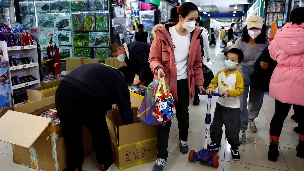 A woman and a child walk past workers sorting toys at a shopping mall in Beijing, China January 11, 2023. REUTERS/Tingshu Wang