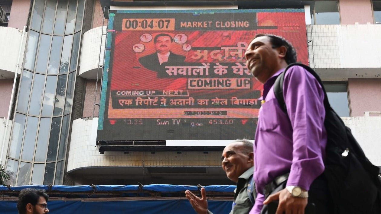 People walk past an electronic signage displaying news on the Adani Group at the Bombay Stock Exchange (BSE) building in Mumbai on January 27, 2023. - Trading in the business empire of Asia's richest man Gautam Adani was halted on January 27, 2023 following a 15 percent plunge in its share price, days after a US investment firm claimed it had committed brazen corporate fraud. (Photo by SUJIT JAISWAL / AFP)